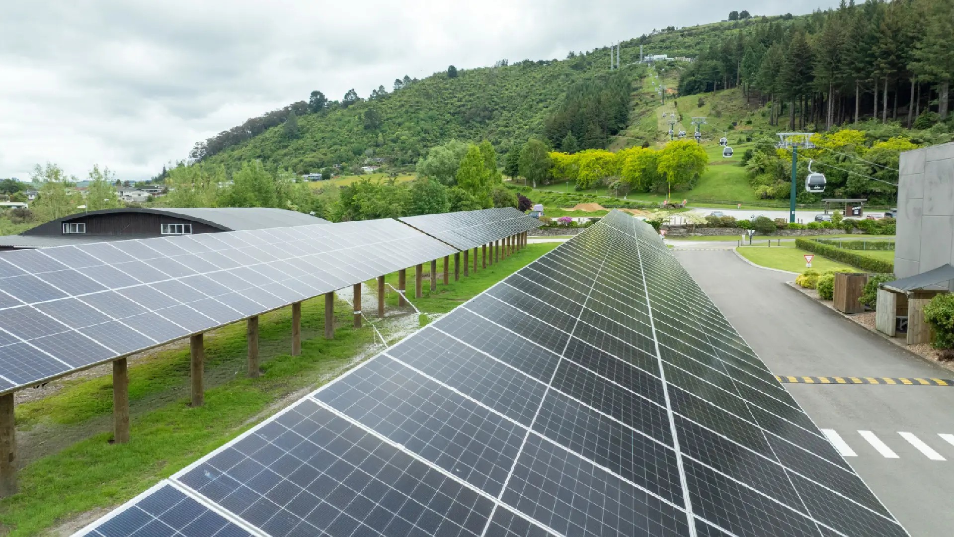Ground-mounted solar panel arrays at Skyline Rotorua with gondola cabins and forested hillside in the background.
